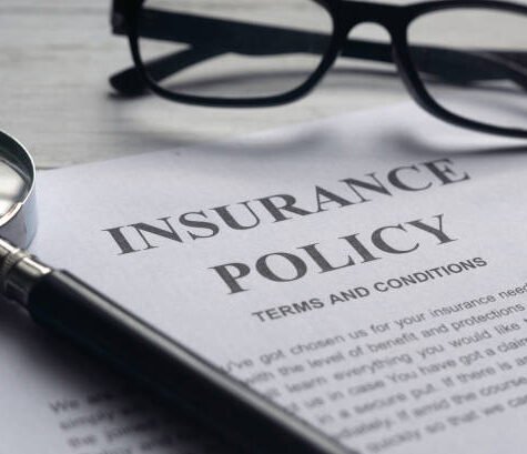 Selective focus of magnifying glass,glasses and Insurance Policy letter on a white wooden background.